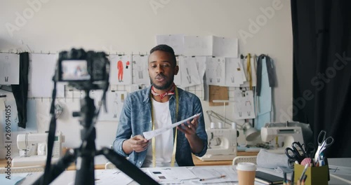 Male fashion designer vlogger recording video for internet blog showing sketches speaking and gesturing working in studio alone. People and vlogging concept. photo