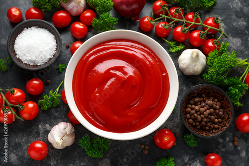 Homemade ketchup sauce in white bowl with vegetables and herbs