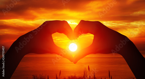  Heart shaped female hands silhouette with sunset background