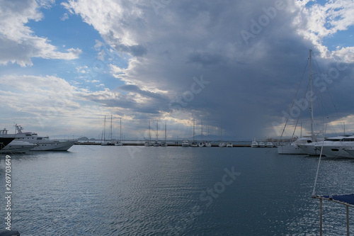 Amazing view at sea port with boats and heavy clouds on blue sky. Seascape before a thunderstorm. Beautiful white modern yachts and boats are at sea port in Spain.