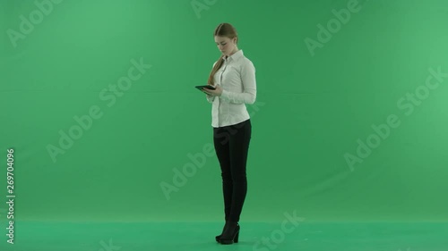 Young business woman is chating on her tablet. She wears formal dress: white shirt and blak trousers and stands on the green screen. photo