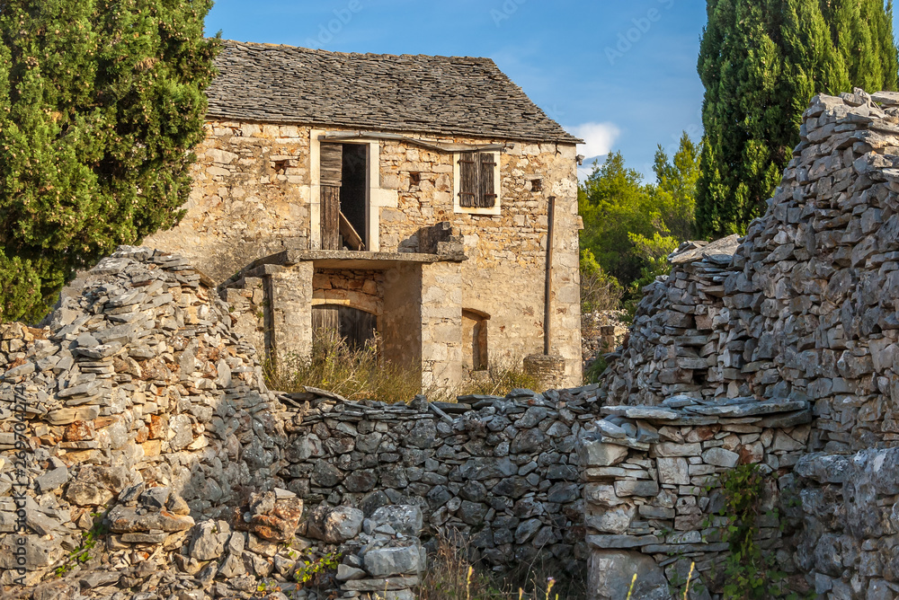 An old stone abandoned house, in front of it there are remains of another stone house. The uninhabited village of Humac, Hvar Island, Croatia.
