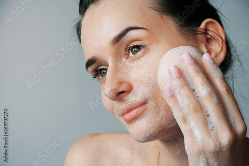 girl cleans face with foam and sponge for washing
