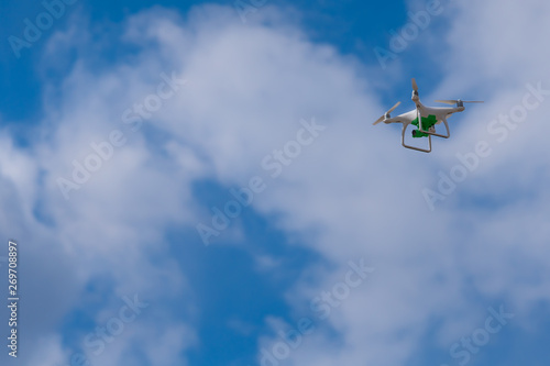 White drone with a green camera flying against the sky.