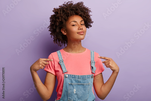 People, pride, arrogance concept. Self assured proud woman has Afro hairstyle satisfied with own high achievements, feels confident, keeps head raised, being like hero, isolated on purple wall