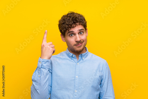 Blonde man over isolated yellow wall pointing with the index finger a great idea