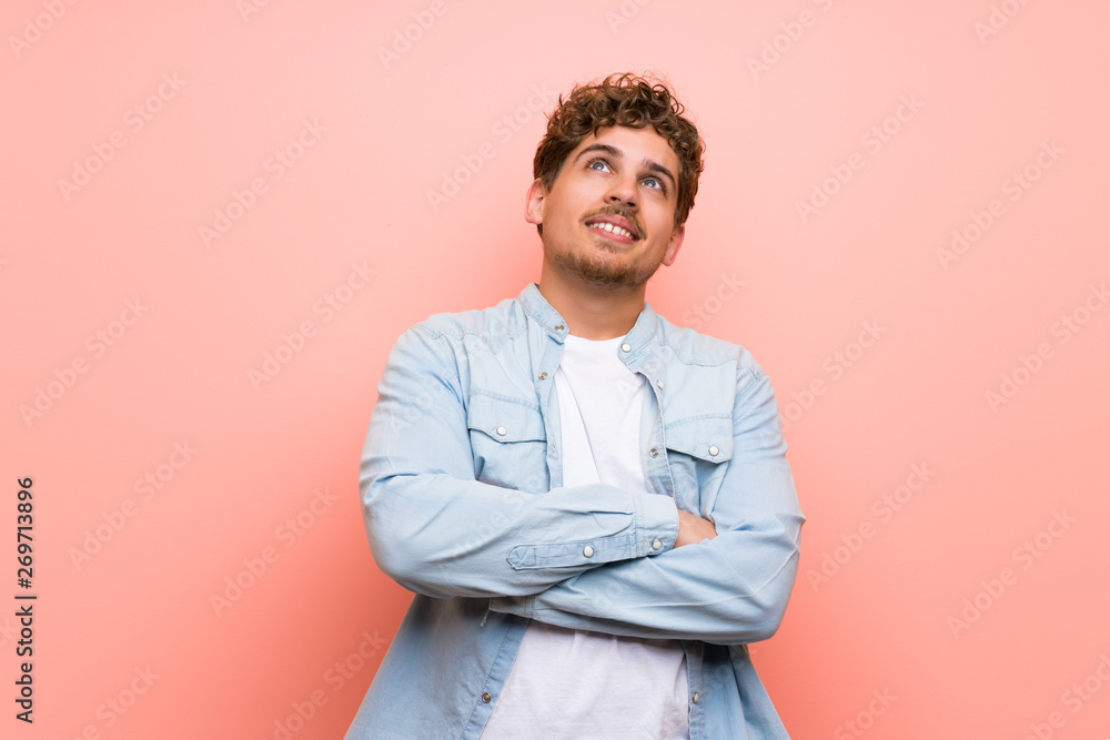 Blonde man over pink wall looking up while smiling Blonde man over pink wall looking up while smiling