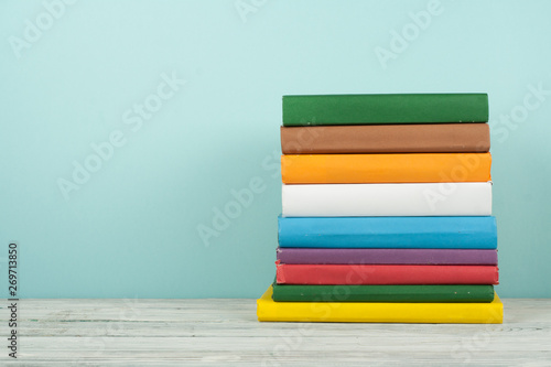 Book stack, hardback colorful books on wooden table and blue background. Back to school. Copy space for text. Education concept.