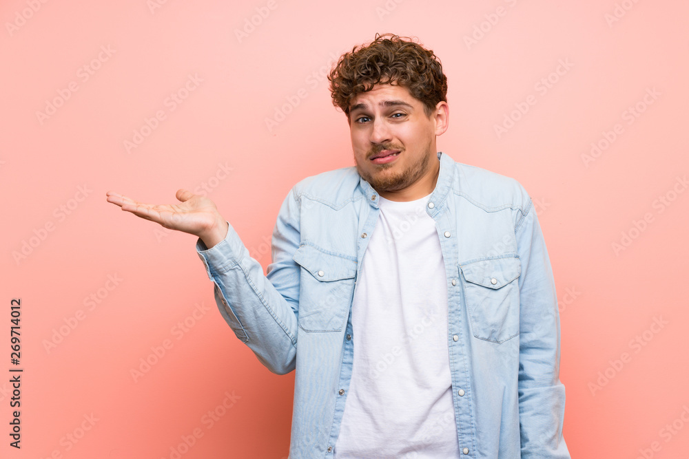 Blonde man over pink wall serious while holding copyspace imaginary Blonde man over pink wall serious while holding copyspace imaginary