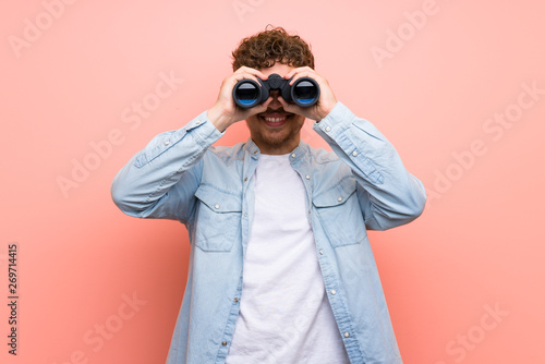 Blonde man over pink wall and looking in the distance with binoculars photo