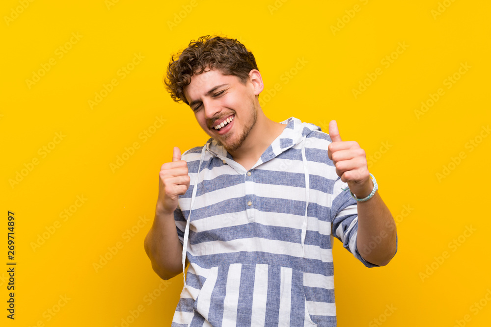 Blonde man over yellow wall enjoy dancing while listening to music at a party Blonde man over yellow wall enjoy dancing while listening to music at a party