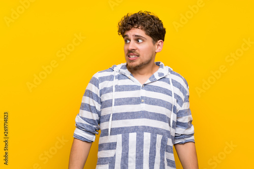 Blonde man over yellow wall is a little bit nervous and scared pressing the teeth