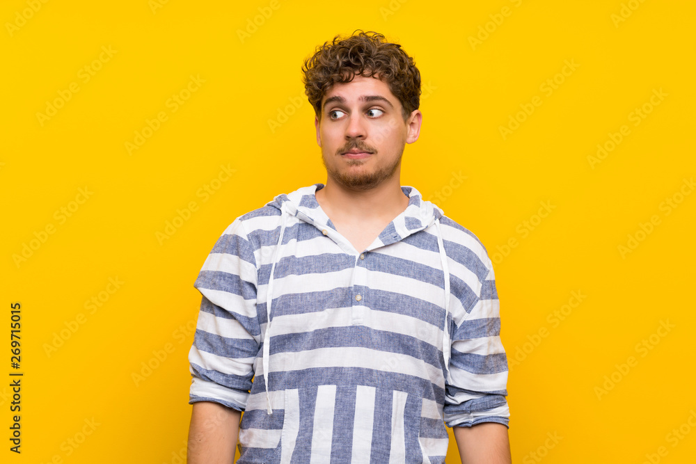 Blonde man over yellow wall making unimportant gesture Blonde man over yellow wall making unimportant gesture