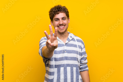 Blonde man over yellow wall happy and counting three with fingers