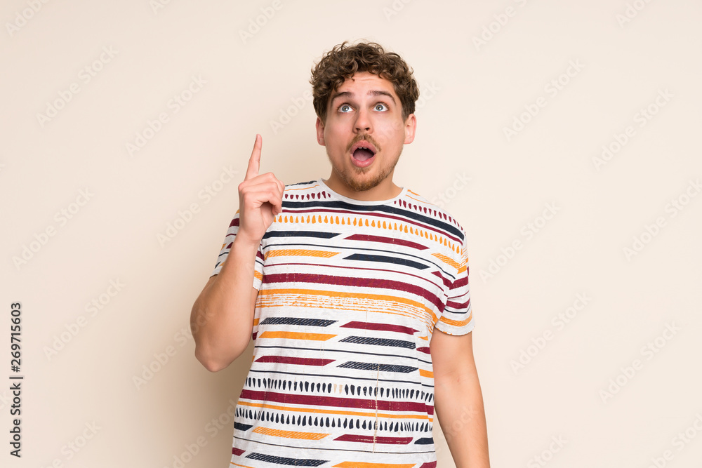 Blonde man over isolated wall pointing up and surprised Blonde man over isolated wall pointing up and surprised