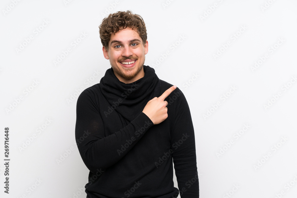 Blonde man over isolated white wall pointing to the side to present a product Blonde man over isolated white wall pointing to the side to present a product