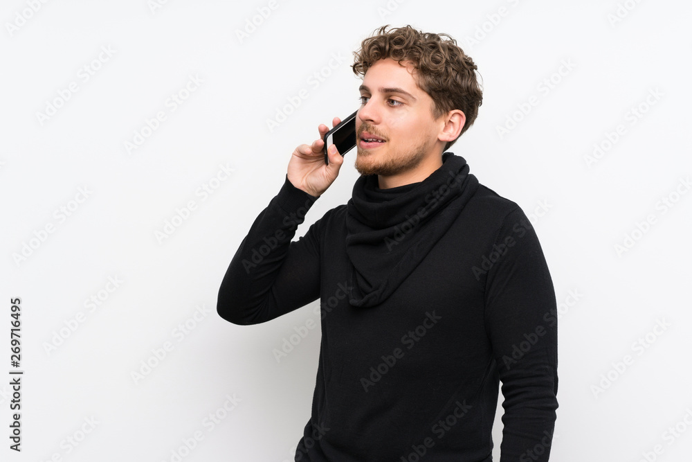 Blonde man over isolated white wall keeping a conversation with the mobile phone Blonde man over isolated white wall keeping a conversation with the mobile phone