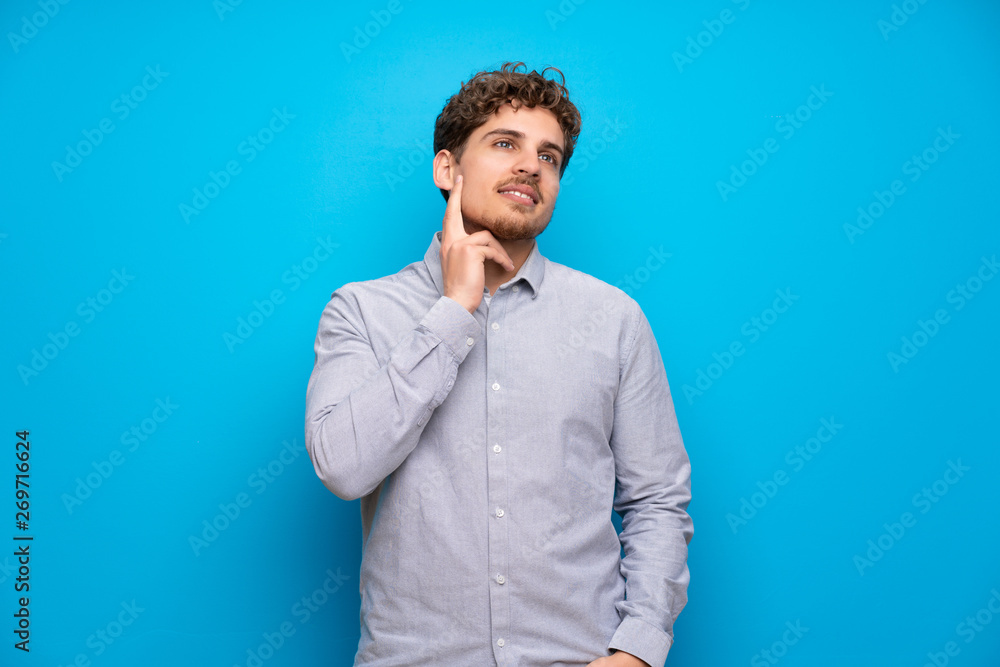 Blonde man over blue wall thinking an idea while looking up Blonde man over blue wall thinking an idea while looking up