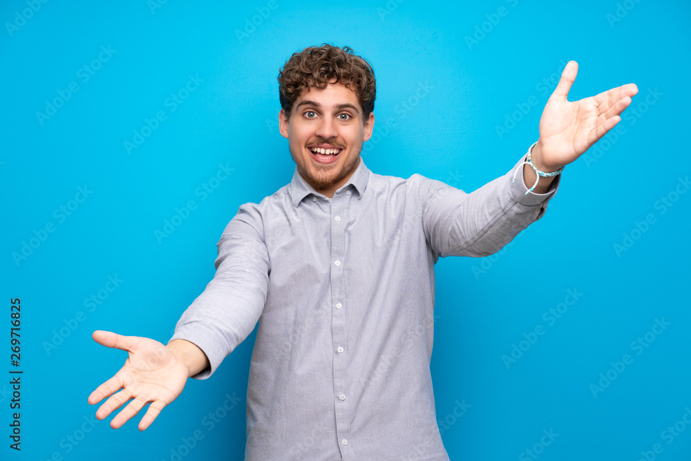 Fototapeta premium Blonde man over blue wall presenting and inviting to come with hand