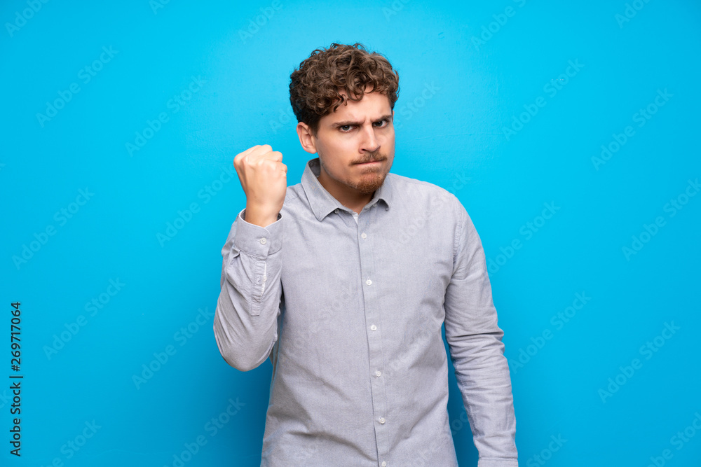Blonde man over blue wall with angry gesture Blonde man over blue wall with angry gesture