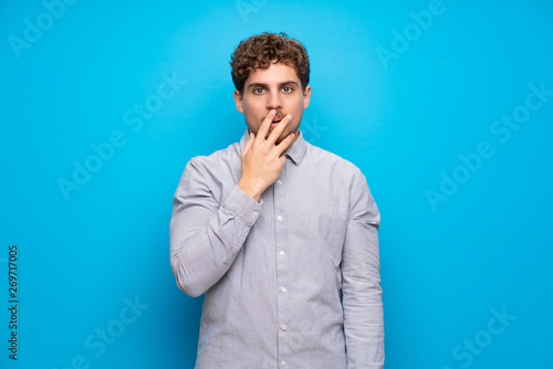 Blonde man over blue wall surprised and shocked while looking right