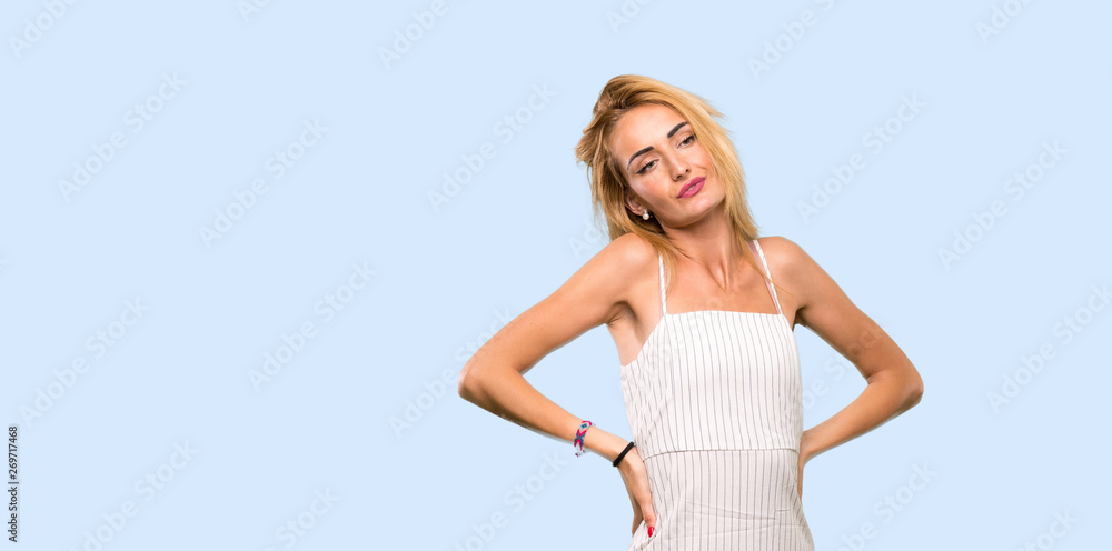 Young blonde woman suffering from backache for having made an effort over isolated blue background Young blonde woman suffering from backache for having made an effort over isolated blue background