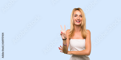 Young blonde woman smiling and showing victory sign over isolated blue background