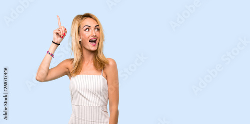 Young blonde woman intending to realizes the solution while lifting a finger up over isolated blue background