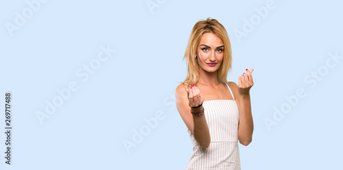 Young blonde woman making money gesture over isolated blue background