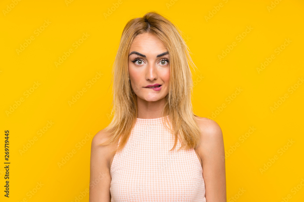 Young blonde woman over isolated yellow wall having doubts and with confuse face expression Young blonde woman over isolated yellow wall having doubts and with confuse face expression