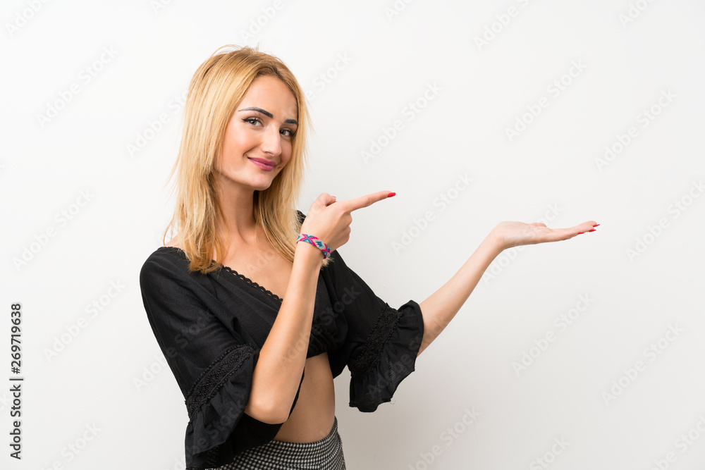 Young blonde woman over isolated white wall holding copyspace imaginary on the palm to insert an ad Young blonde woman over isolated white wall holding copyspace imaginary on the palm to insert an ad