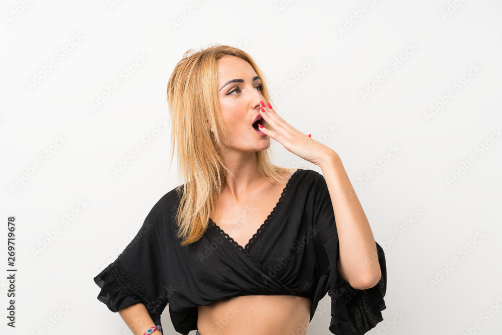 Young blonde woman over isolated white wall yawning and covering wide open mouth with hand Young blonde woman over isolated white wall yawning and covering wide open mouth with hand
