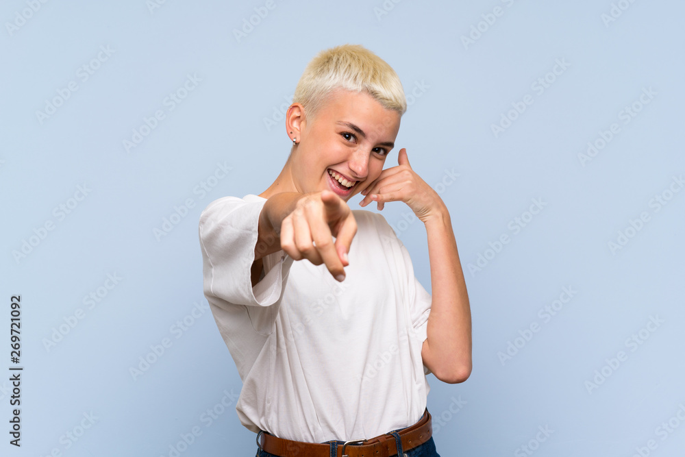 Teenager girl with white short hair over blue wall making phone gesture and pointing front Teenager girl with white short hair over blue wall making phone gesture and pointing front