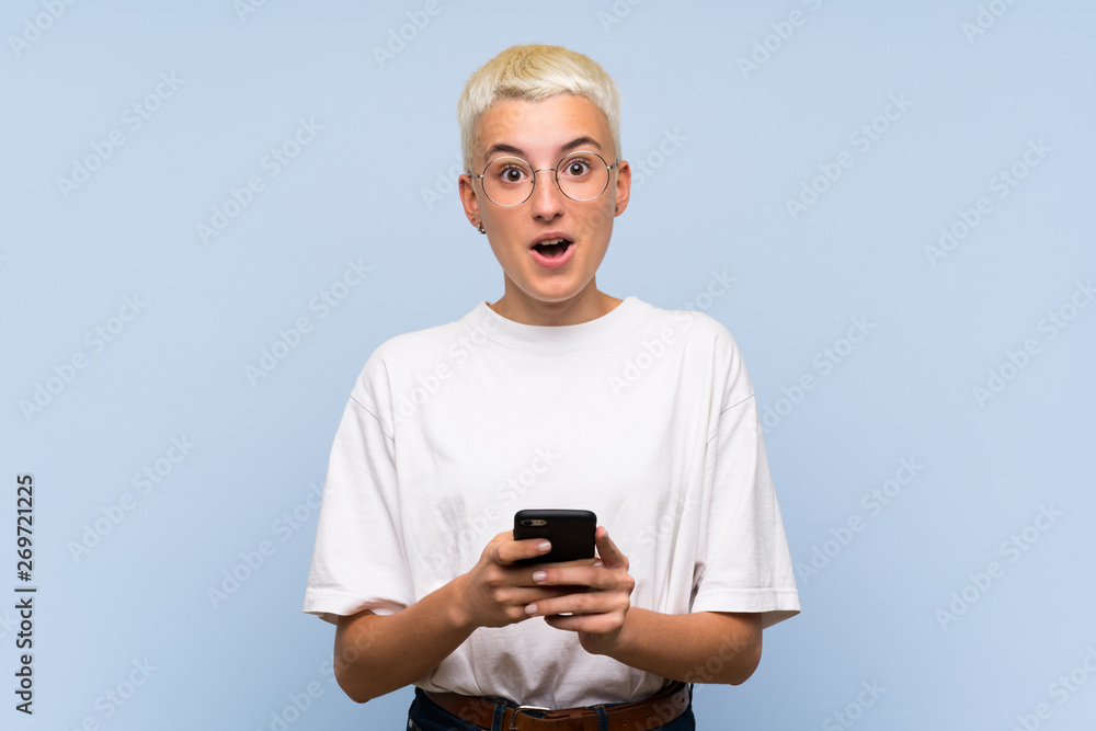 Fototapeta premium Teenager girl with white short hair over blue wall surprised and sending a message