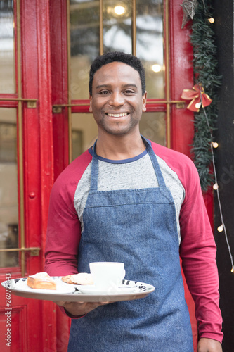 Young waiter brings coffee to customers.