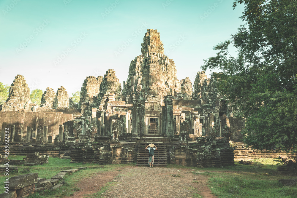 Woman in Bayon Temple looking at stone faces, Angkor Thom, morning light clear blue sky. Buddhism meditation concept, world famous travel destination, Cambodia tourism. Toned vintage