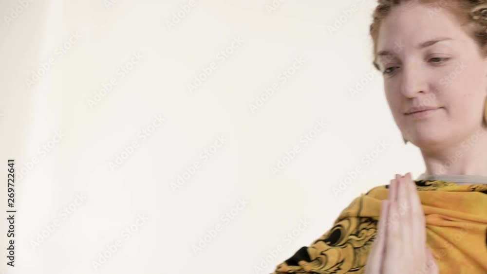 A girl with dreadlocks and hands in bracelets in a gesture of namaste and namaskar. The girl in an authentic scarf practicing meditation standing in the studio on a white background A girl with dreadlocks and hands in bracelets in a gesture of namaste and namaskar. The girl in an authentic scarf practicing meditation standing in the studio on a white background