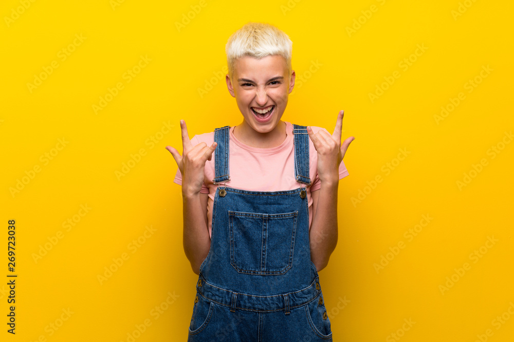 Teenager girl with overalls on yellow background making rock gesture Teenager girl with overalls on yellow background making rock gesture