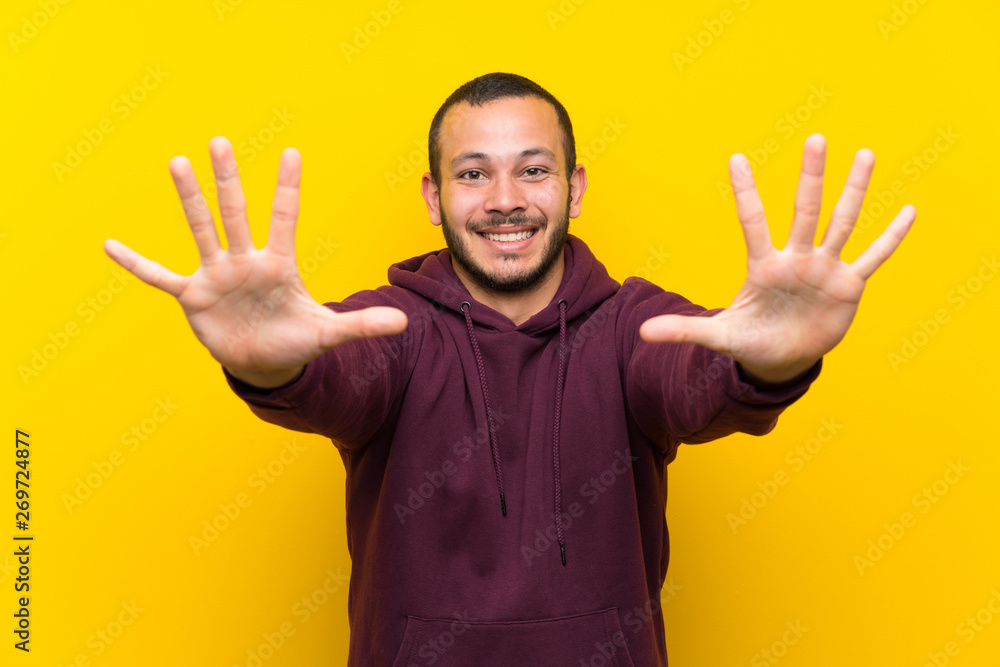 Colombian man with sweatshirt over yellow wall counting ten with fingers Colombian man with sweatshirt over yellow wall counting ten with fingers