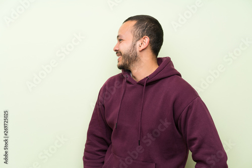 Colombian man with sweatshirt over green wall looking to the side