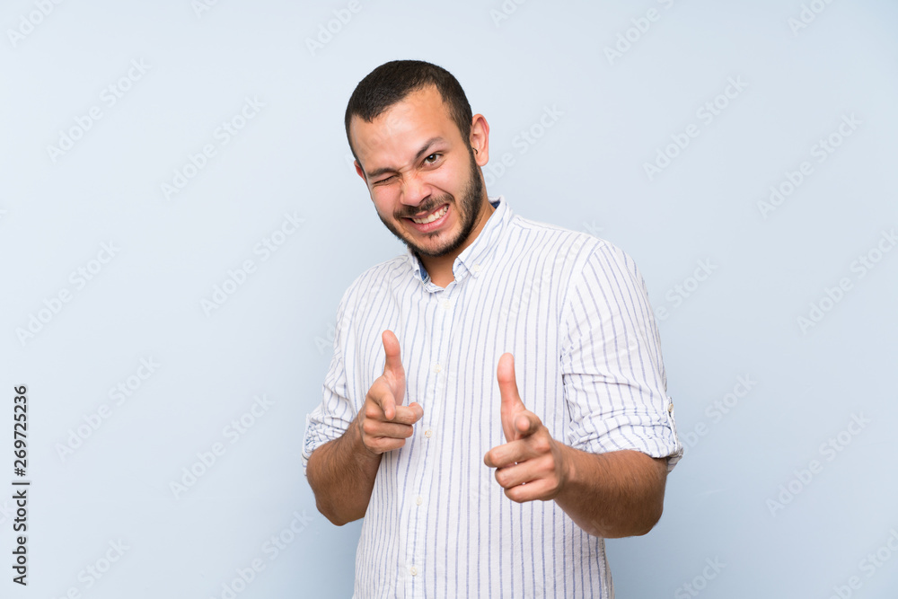 Colombian man over isolated blue wall pointing to the front and smiling Colombian man over isolated blue wall pointing to the front and smiling