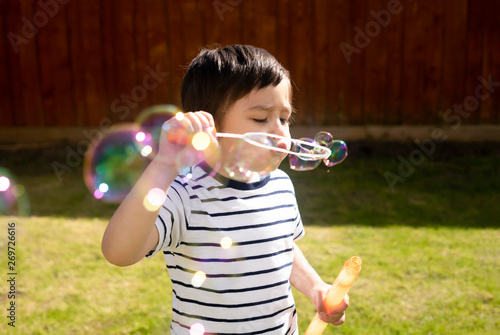 Happy boy blowing soap bubbles in the garden,Cute 4 years old kid blowing bubble wand with a funny face,Cute kid playing in the garden on a sunny summer day,Outdoor activities for Children