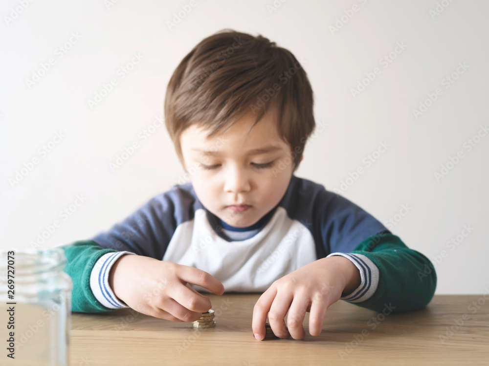 Selective focus of Kid boy couthing coins pond on the table, Blurry child face playing with coins making stacks of money, children saving money for the future concept Selective focus of Kid boy couthing coins pond on the table, Blurry child face playing with coins making stacks of money, children saving money for the future concept