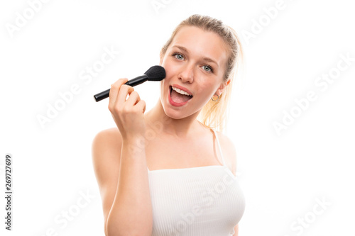 Young blonde woman over isolated white background with makeup brush