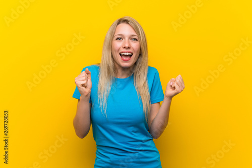 Young blonde woman over isolated yellow background celebrating a victory in winner position
