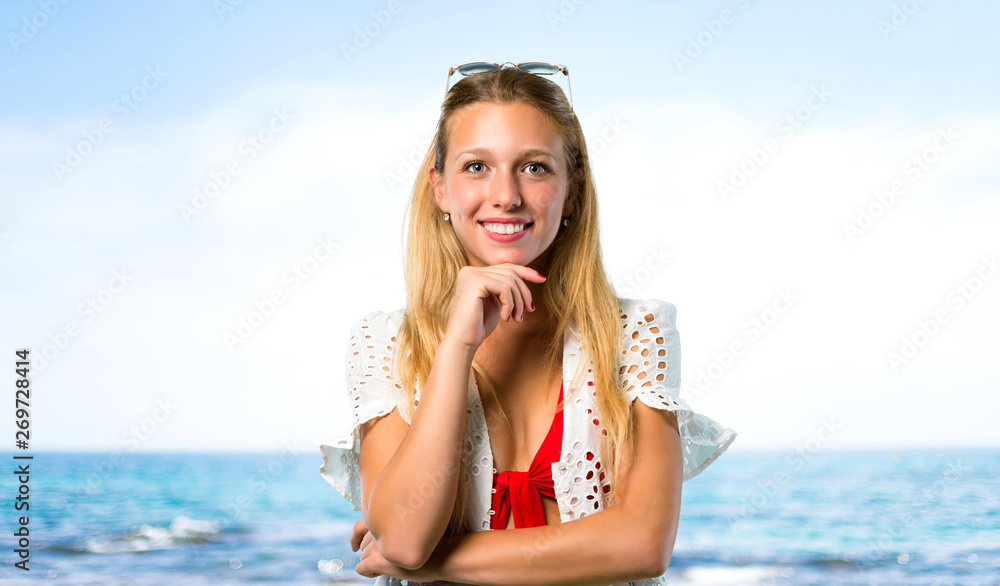 Blonde girl in summer vacation smiling and looking to the front with confident face at the beach