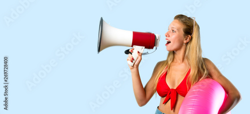 Blonde woman in summer vacation holding a megaphone on blue background