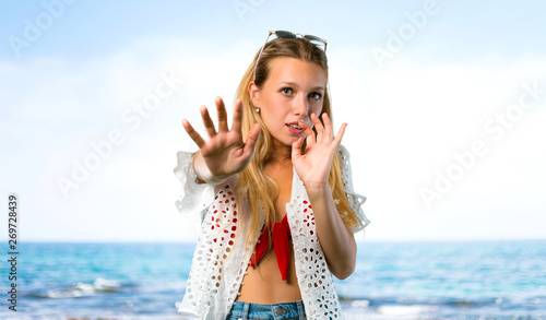 Blonde girl in summer vacation is a little bit nervous and scared stretching hands to the front at the beach © luismolinero