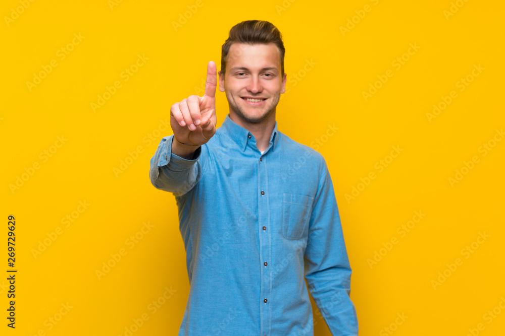 Blonde man over isolated yellow wall showing and lifting a finger Blonde man over isolated yellow wall showing and lifting a finger