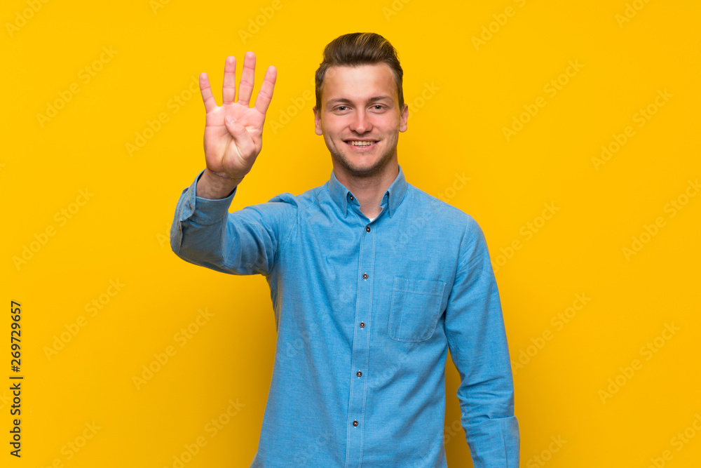Blonde man over isolated yellow wall happy and counting four with fingers Blonde man over isolated yellow wall happy and counting four with fingers